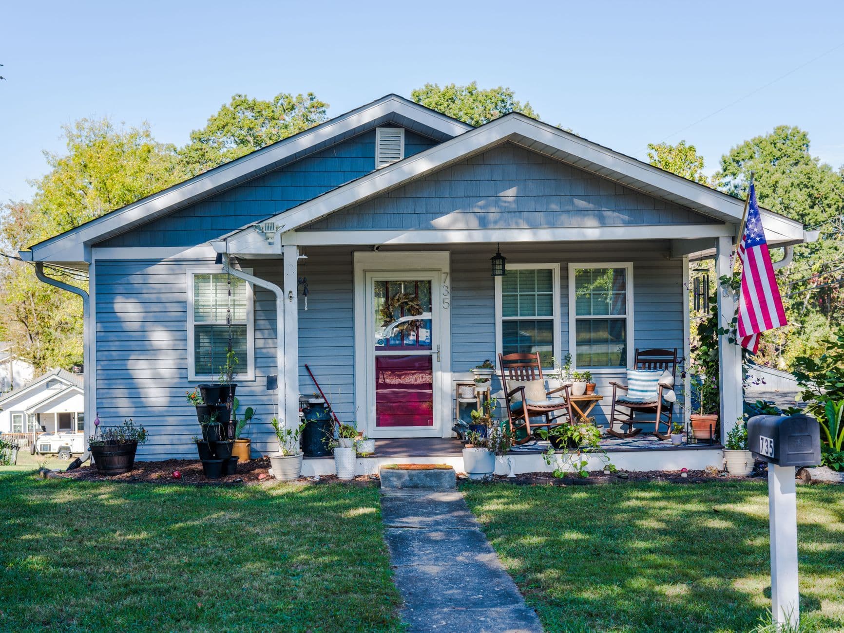 Charming blue house with porch seats and American flag in a suburban neighborhood.